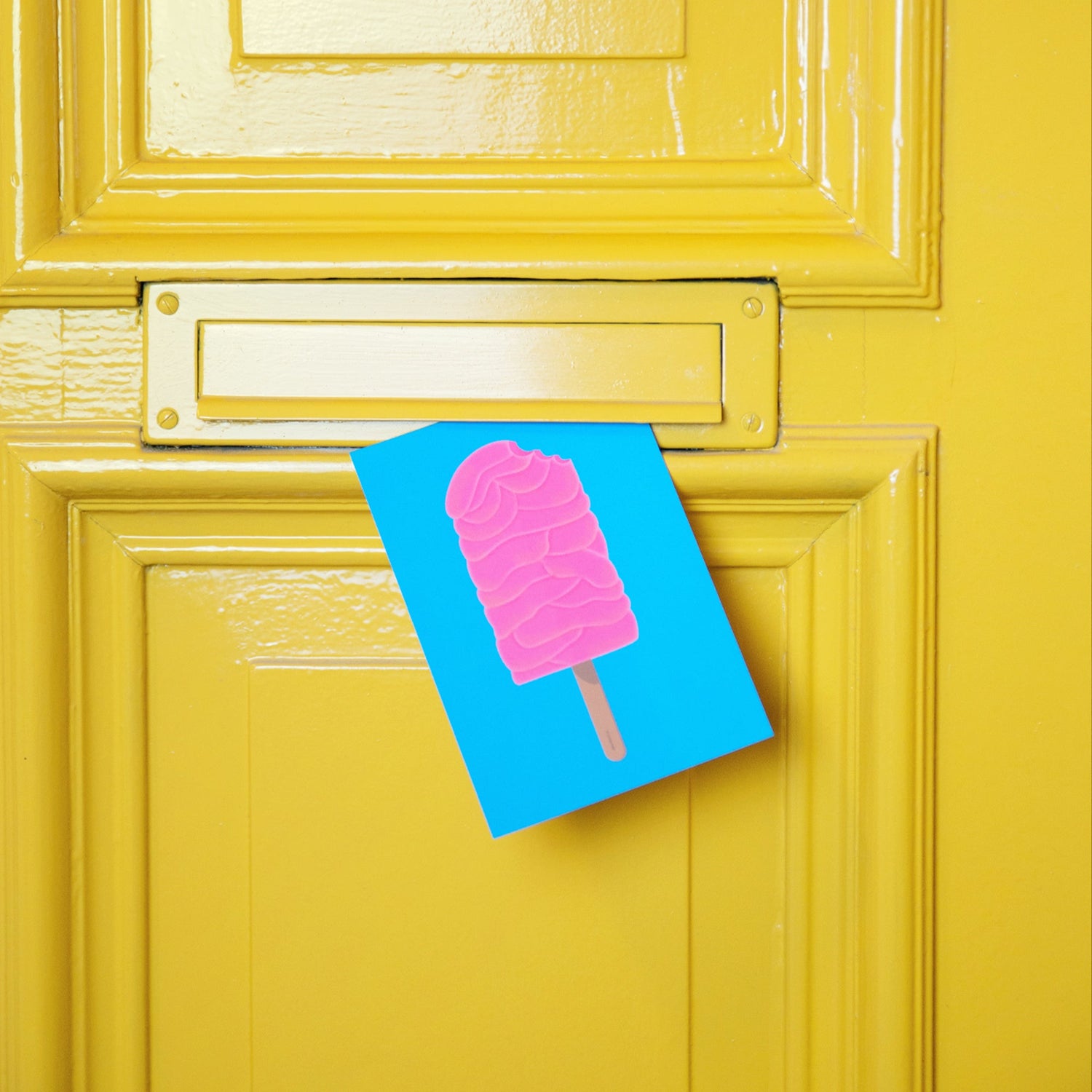 Postkarte »Brainsicle« steckt im Briefschlitz einer gelben Wohnungstür